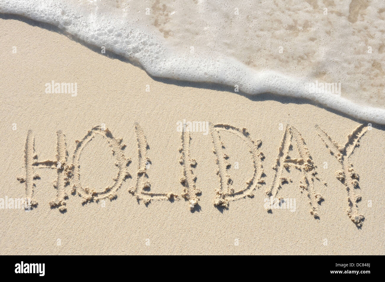 Das Wort "Urlaub" an einem Strand in den Sand geschrieben Stockfoto