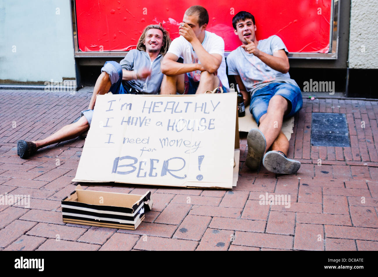 Drei Männer betteln um Geld mit Schild mit der Aufschrift "Ich bin gesund, ich habe ein Haus. Ich brauche Geld für Bier! " Stockfoto