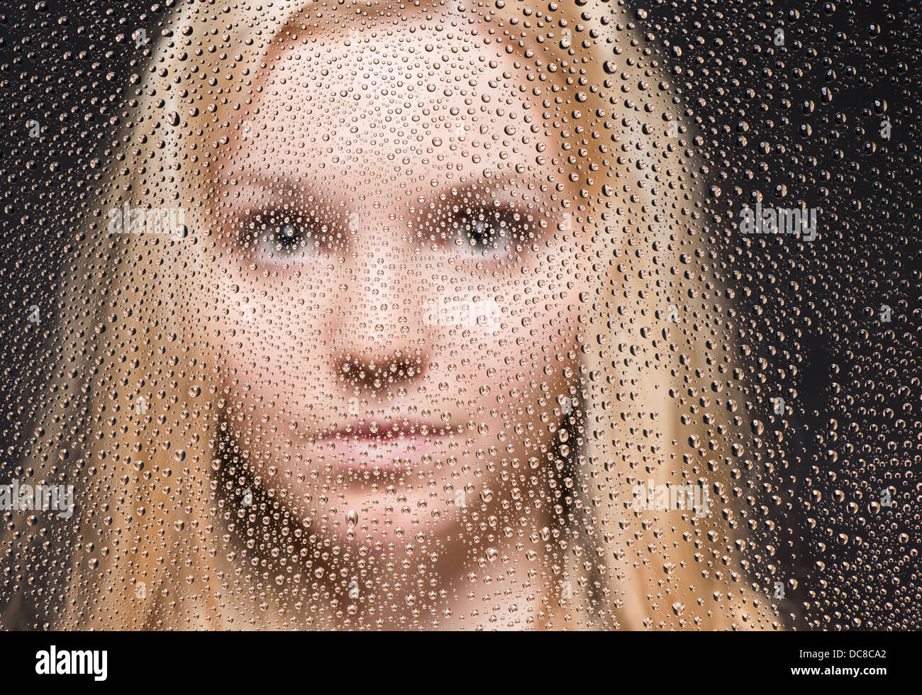 Porträt der jungen blonden weiblichen Teenager Blick aus Fenster bedeckt mit Regentropfen Stockfoto
