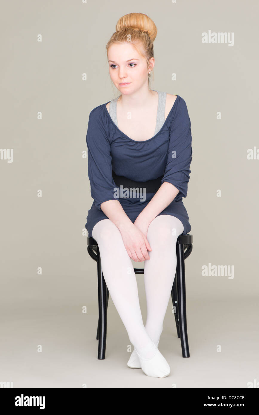 Nachdenkliche junge blonde weibliche Teenager im Ballett Kleid auf Stuhl sitzend Stockfoto