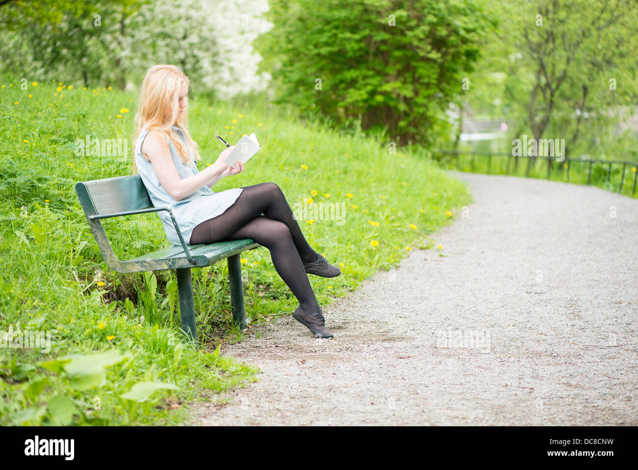 Eine junge attraktive Frau sitzen auf Bank in einem Park in ein Tagebuch zu schreiben Stockfoto