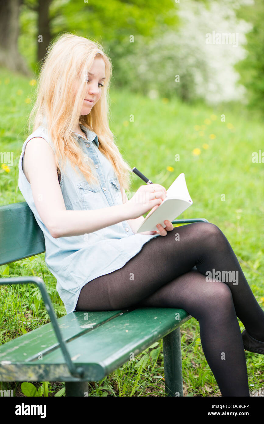 Eine junge attraktive Frau sitzen auf Bank in einem Park in ein Tagebuch zu schreiben Stockfoto