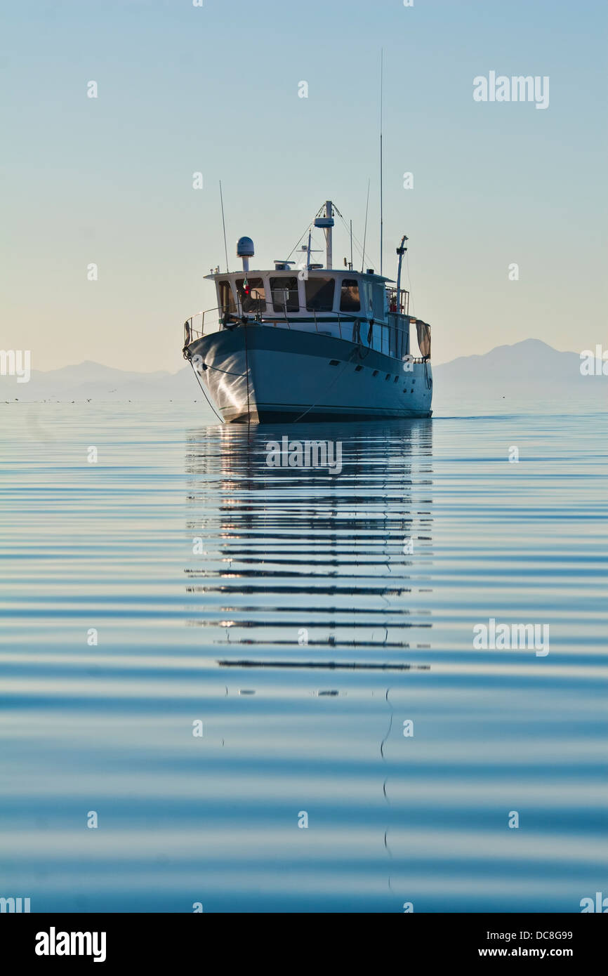 Fischereifahrzeug verankert in ruhigem Wasser mit Bergen hinter dem Boot am Horizont Stockfoto