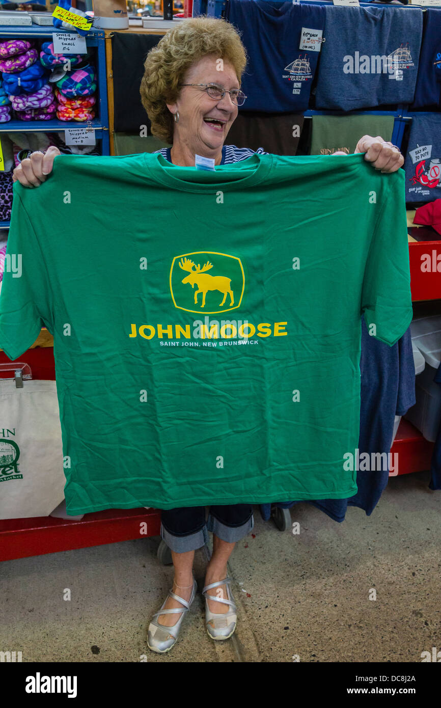 Ältere Verkäuferin nach vorne gerichtet und hält ein "John Moose"-Shirt, eine Mengenermittlung für "John Deere" in einer kanadischen Stadt-Markt. Stockfoto
