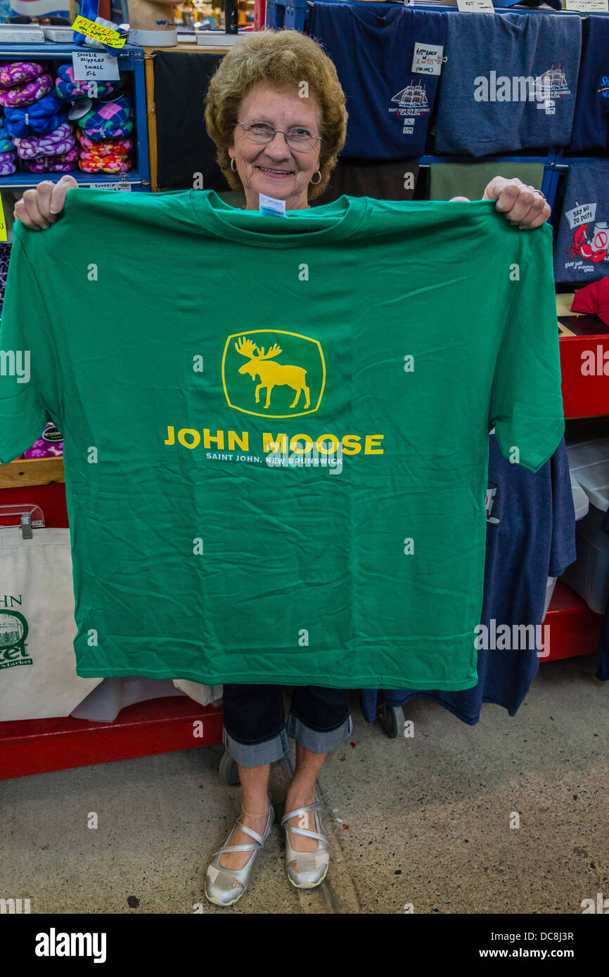 Ältere Verkäuferin nach vorne gerichtet und hält ein "John Moose"-Shirt, eine Mengenermittlung für "John Deere" in einer kanadischen Stadt-Markt. Stockfoto