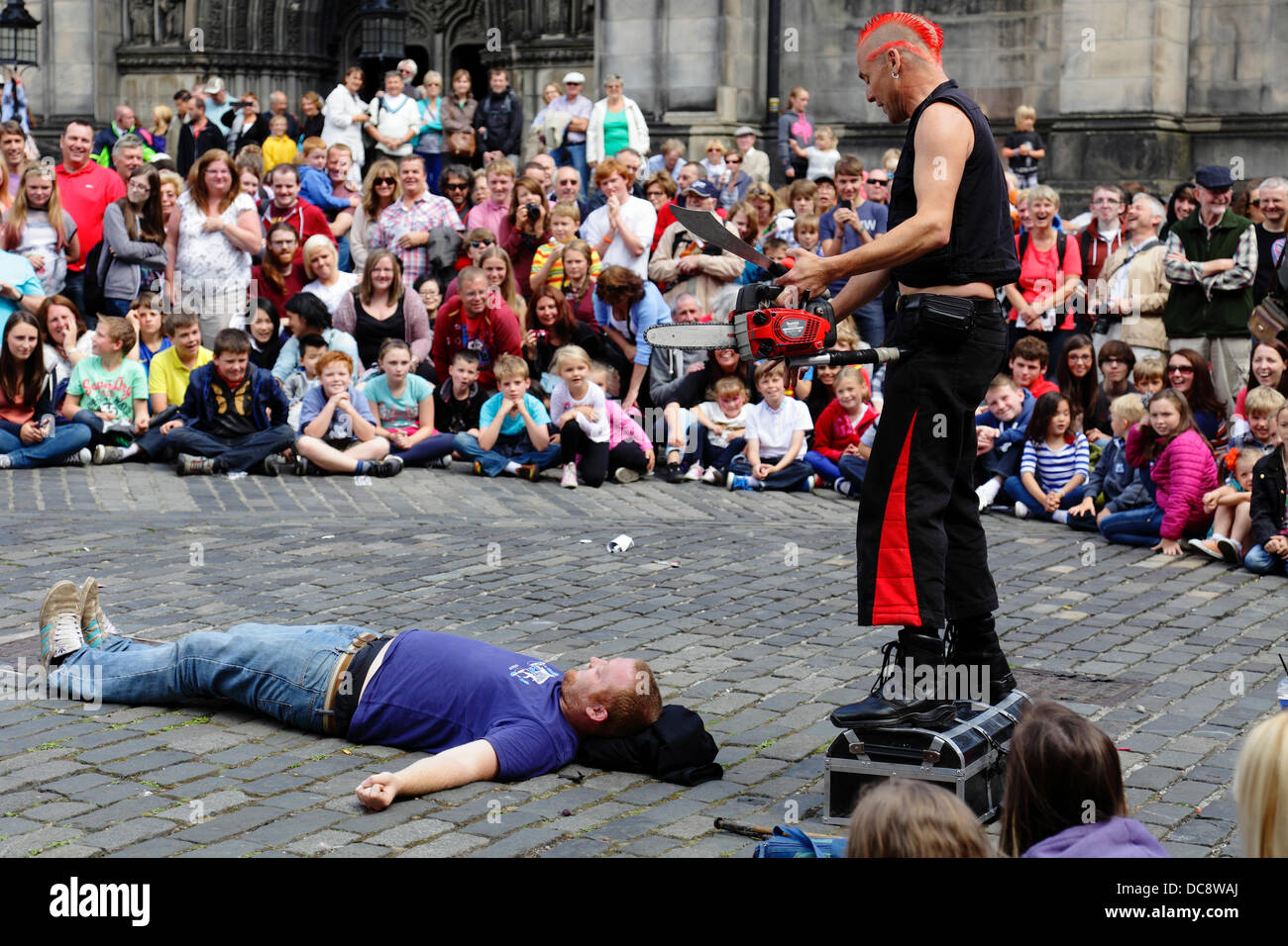 West Parliament Square, Edinburgh City Centre, Schottland, Großbritannien, Montag, 12. August 2013. Street Performer Mighty Gareth bereitet sich darauf vor, während des Edinburgh International Festival Fringe mit einer Kettensäge und einem Messer über einem Freiwilligen aus dem Publikum zu jonglieren Stockfoto