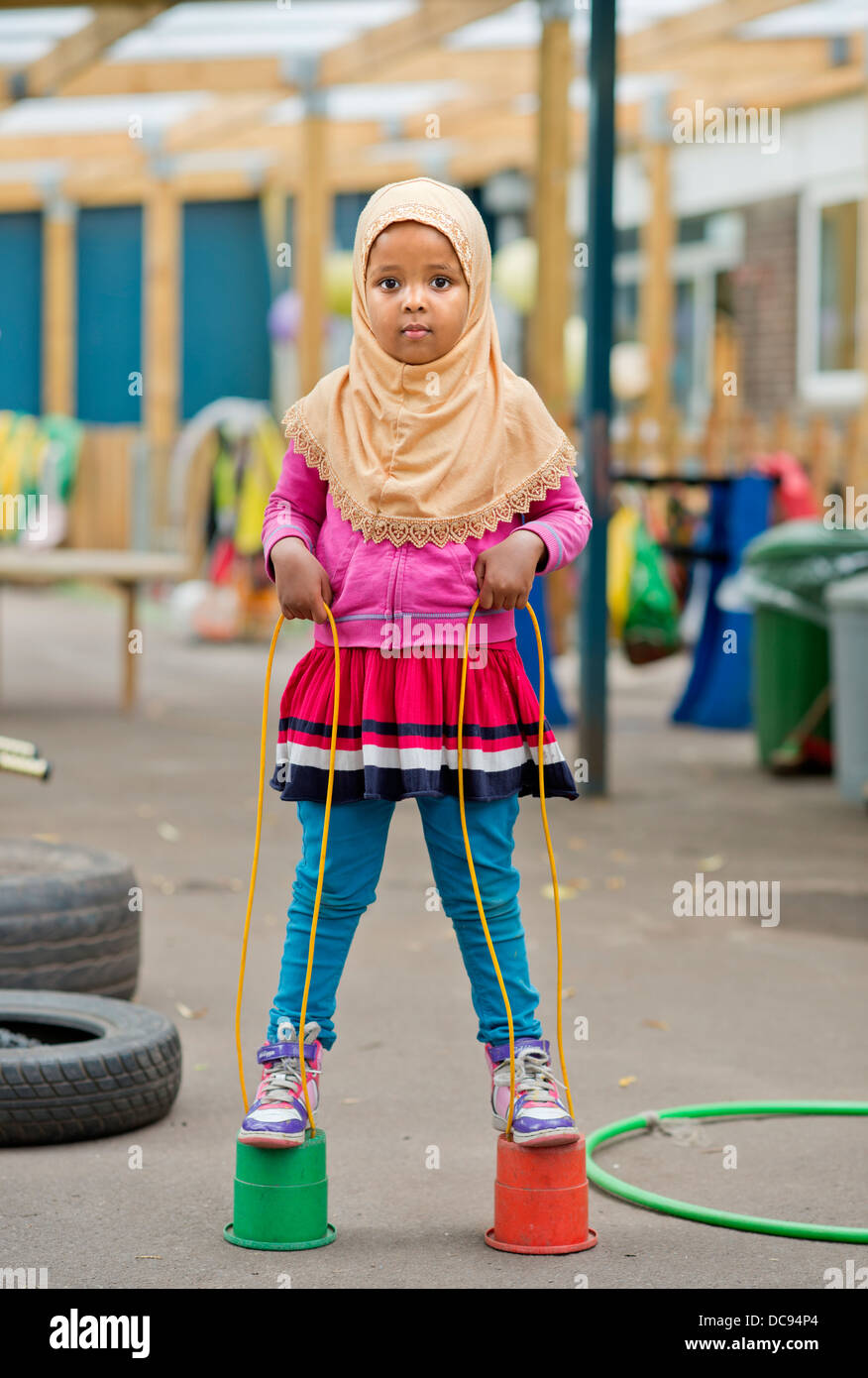 Der St.-Pauls-Kindergarten und das Kinderhaus, Bristol UK - A somalische Mädchen auf Stelzen auf dem Spielplatz spielen. Stockfoto