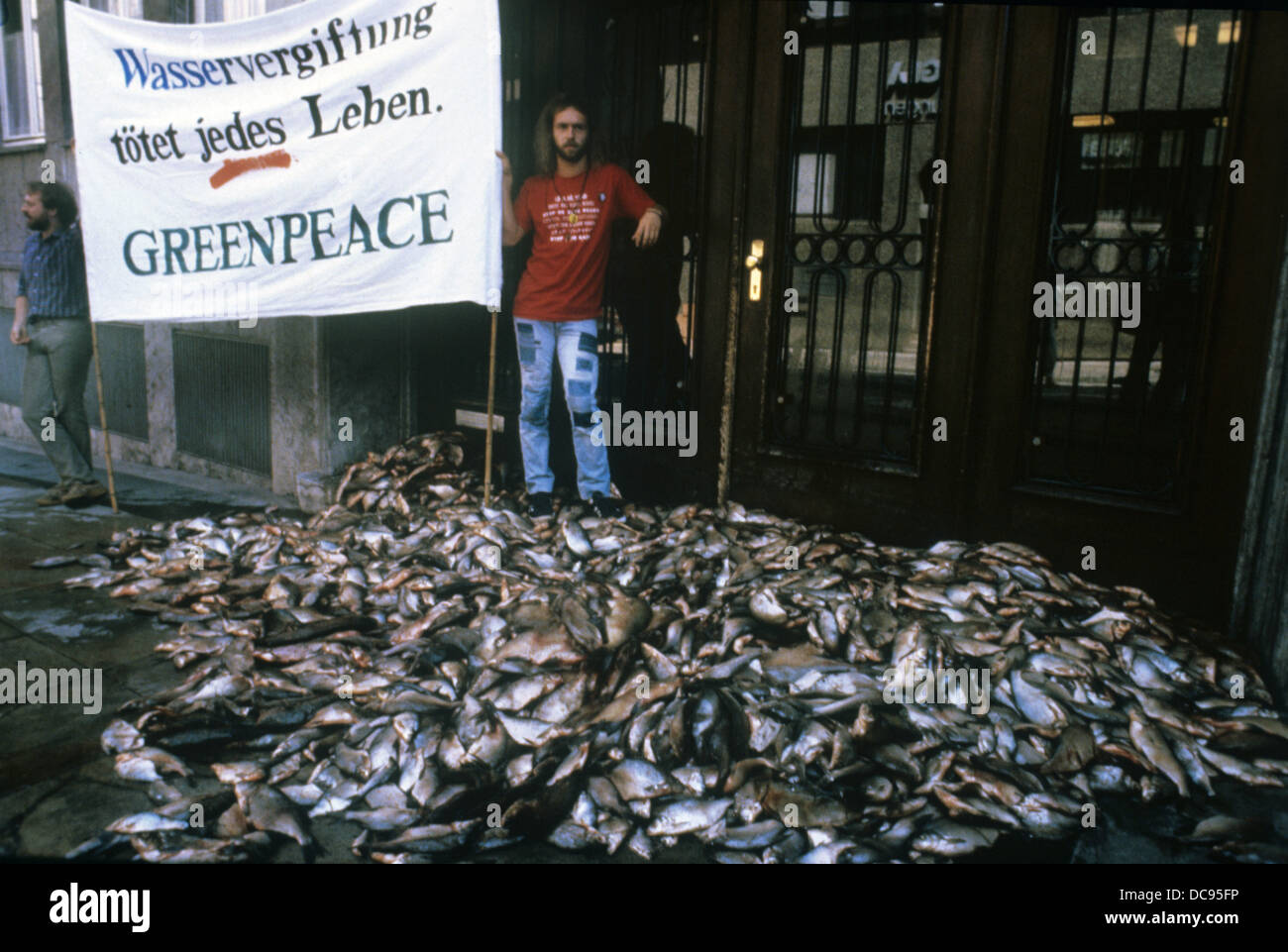 Zwei Mitglieder der Umweltgruppe Greenpeace mit einem Banner und einem Haufen toter Fische an der landwirtschaftlichen Fakultät in Stuttgart am 21. August 1985. Stockfoto