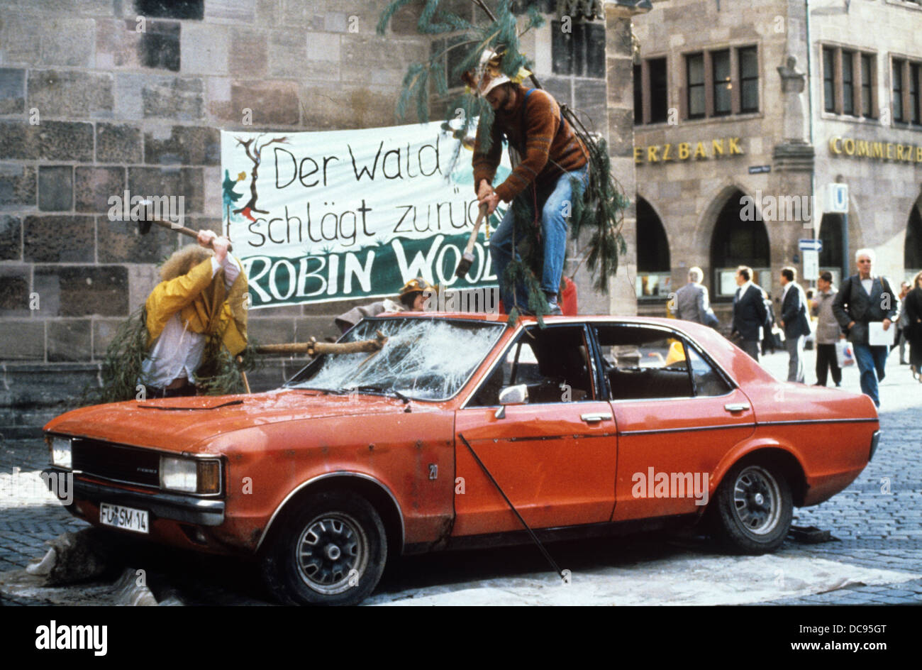Mitglieder der Umweltorganisation Robin Wood als Bäume verkleidet sind und schlagen ein altes Auto als eine Protestaktion gegen das Waldsterben, fotografiert am 9. November 1989. Stockfoto