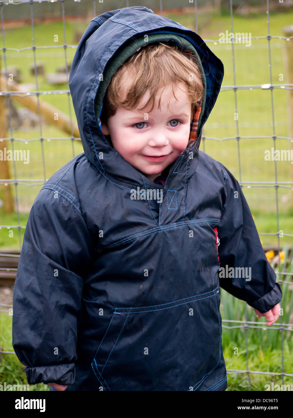 Ein kleiner Junge draußen im Regen eine wasserdichte Jacke mit Kapuze tragen. Stockfoto