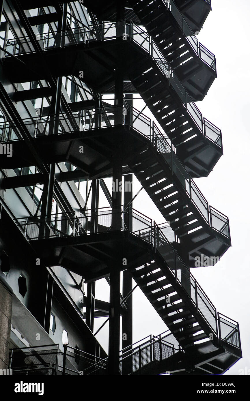 Externe Feuerflut aus schwarzem Stahl, fotografiert vor einem weißen Himmel. Eiserne Treppen. Externer Feuerausweg. Außentreppe. Stockfoto
