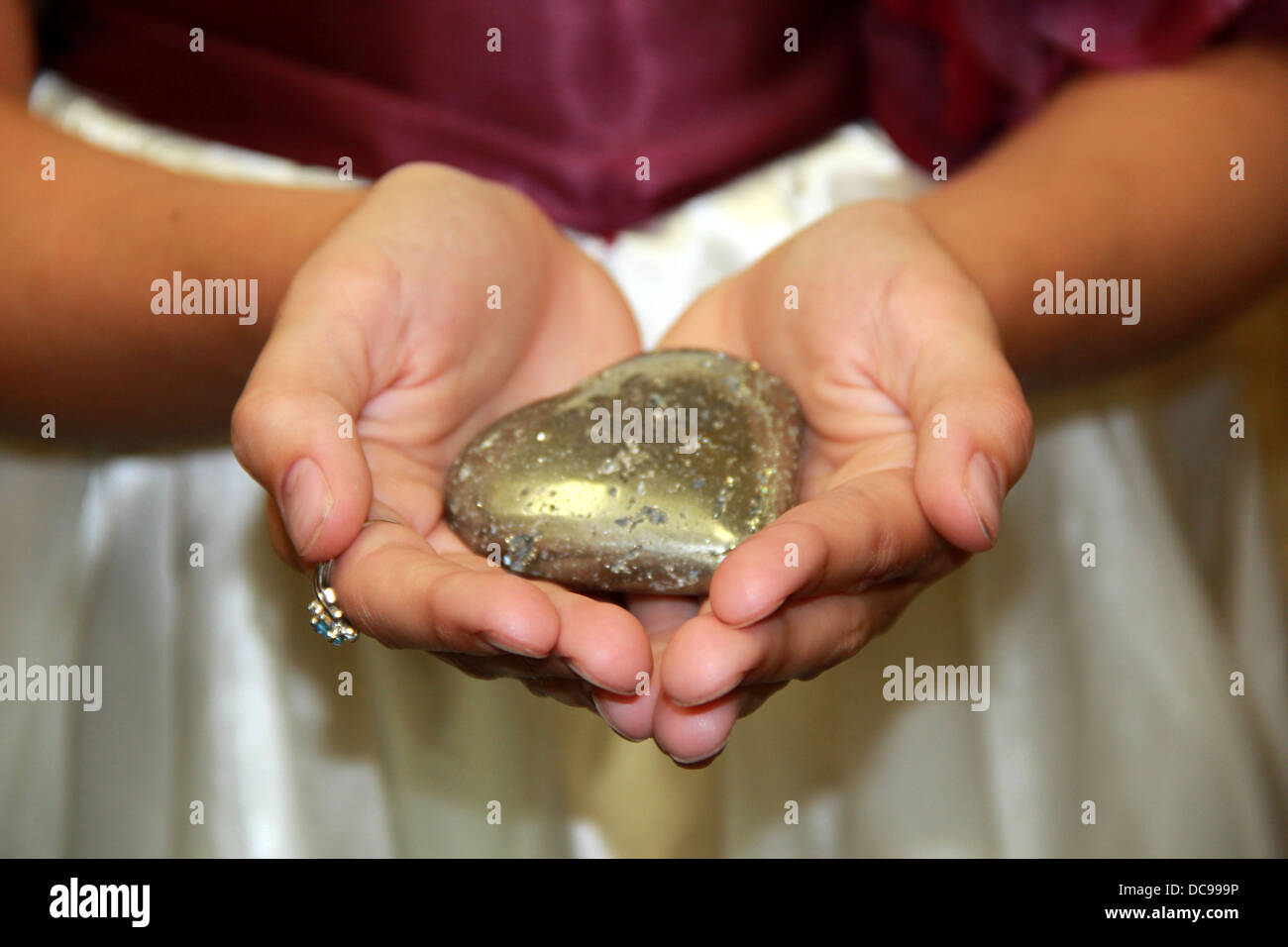 Junges Mädchen offene Hände halten herzförmigen Stein, ein stiller Ausdruck der Liebe für ihre Mutter, die bald heiraten. Stockfoto