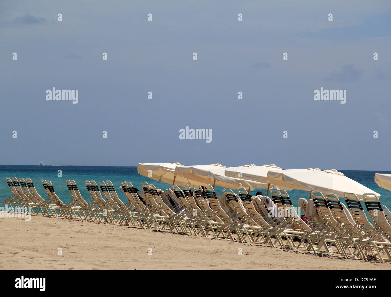 Reihe von schwarzen und weißen Liegestühlen am warmen Sandstrand, mit großen Schatten Sonnenschirmen zum Schutz vor hellen, sonnigen Tag. Stockfoto