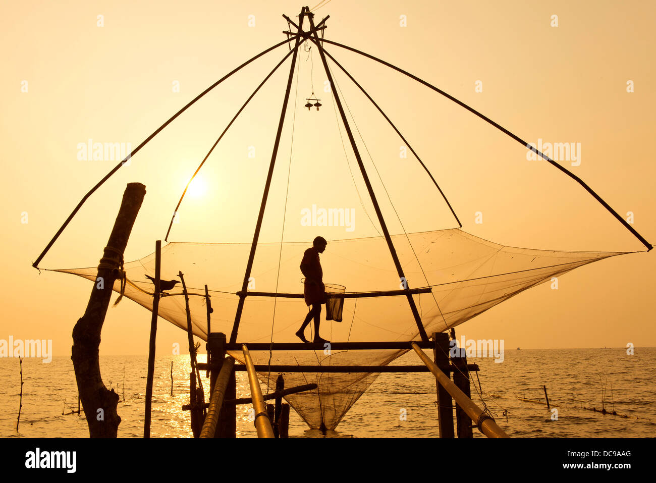 Fischer hält einen Kescher in einem chinesischen Fischernetz bei Sonnenaufgang Stockfoto