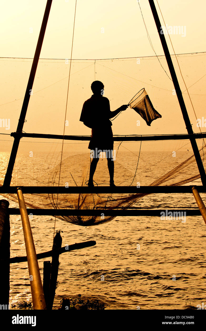 Fischer hält einen Kescher vor einem chinesischen Fischernetz bei Sonnenaufgang Stockfoto
