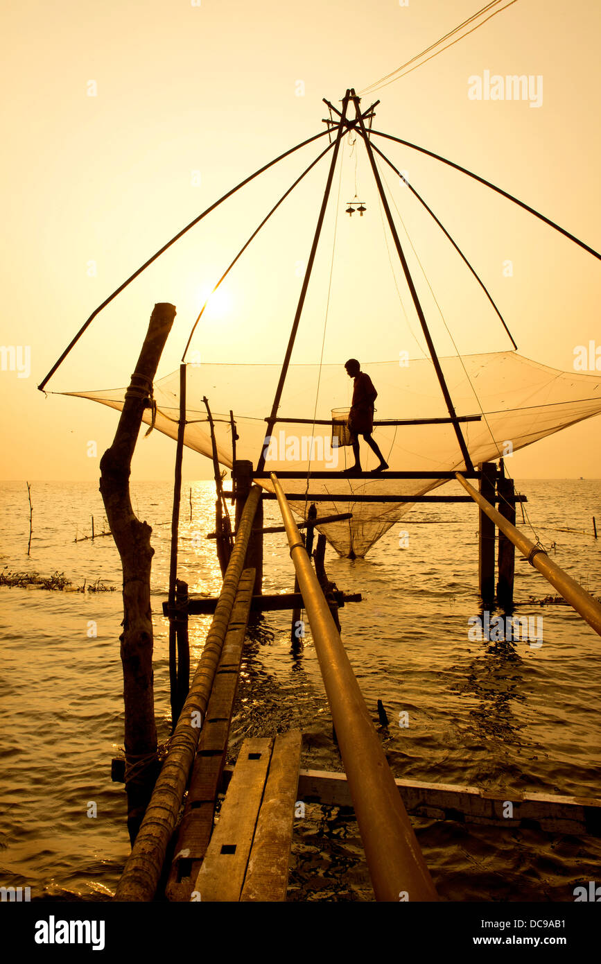 Fischer hält einen Kescher in einem chinesischen Fischernetz bei Sonnenaufgang Stockfoto