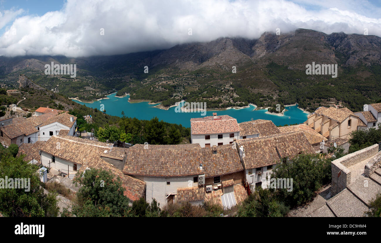 Panorama von Guadalest - ein kleines Dorf, berühmt für seine Burg und Glockenturm. Schwere Wolken liegen die Berge und den blauen See. Stockfoto