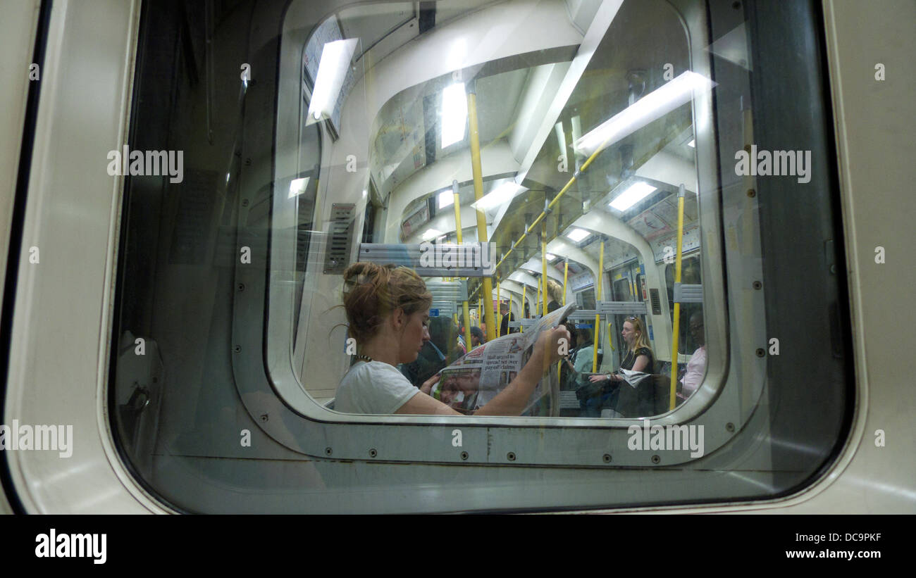 Eine Frau weiblichen Passagier Sitzen auf der U-Bahn eine Zeitung lesen Durch eine Beförderung Fenster London UK KATHY DEWITT gesehen Stockfoto