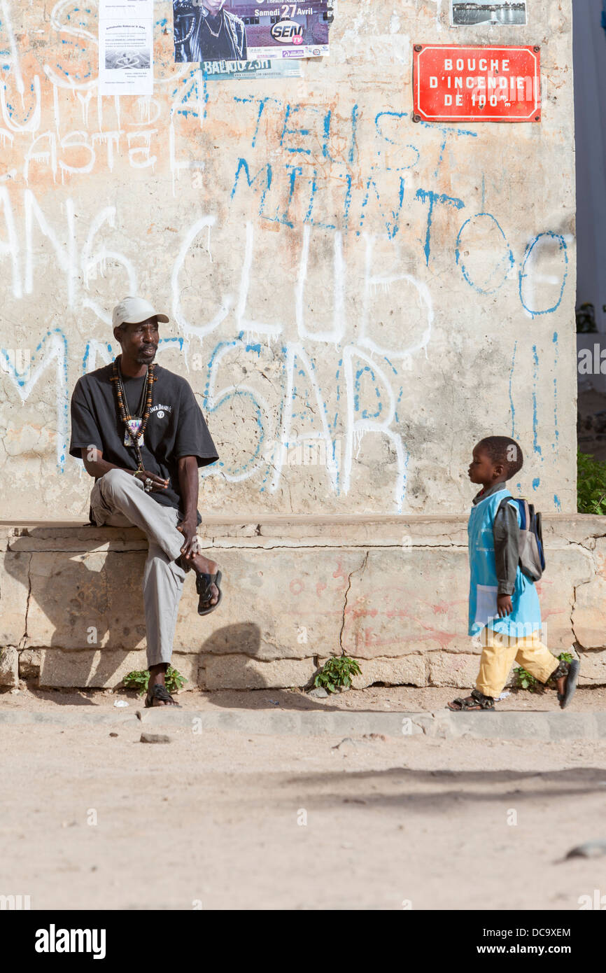 Mann sitzt auf steinernen Gesims ruht, Schüler zu Fuß durch, Goree Island, Senegal. Stockfoto
