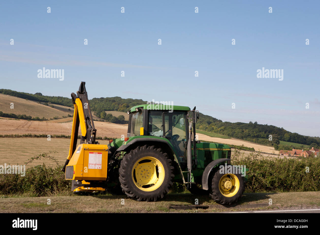 Grün und gelb John Deer Traktor mit Hecke schneiden Arm in Aktion Schneiden einer Hecke am Rande eines Feldes in Oxfordshire, Vereinigtes Königreich. Stockfoto