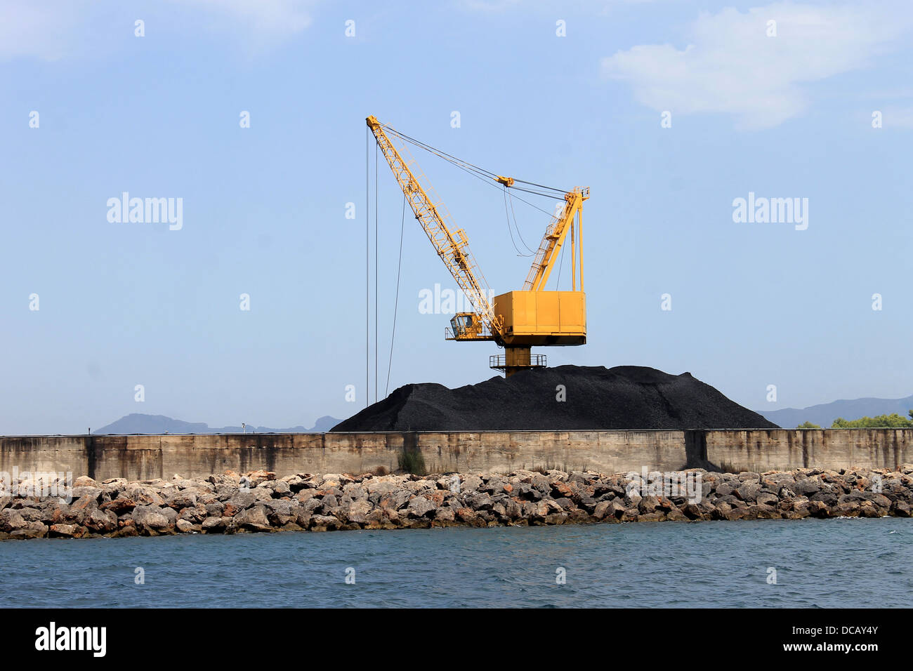 Panoramablick auf gelben Industriekran und Haufen Kohle auf Docks, Hafen von Alcudia, Mallorca, Spanien. Stockfoto