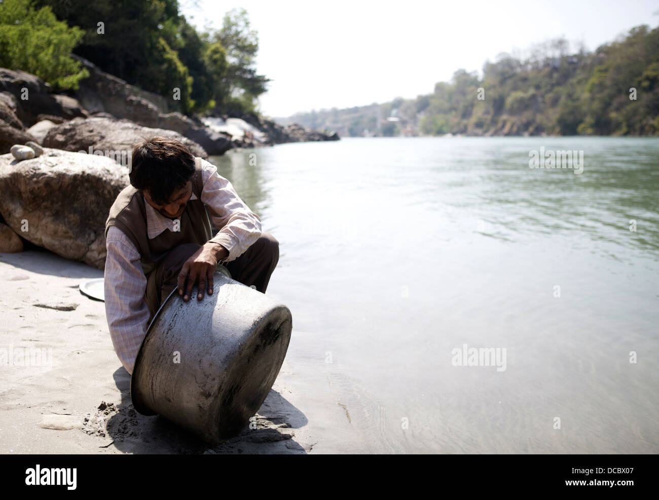 Ein indischer Mann reinigt einen großen Kochtopf in den Fluss Ganges in Rishikesh, Indien. Stockfoto