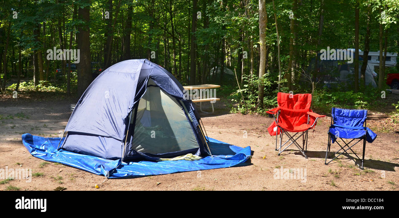 Campingplatz mit Stühlen und Zelt unter Bäumen Stockfoto