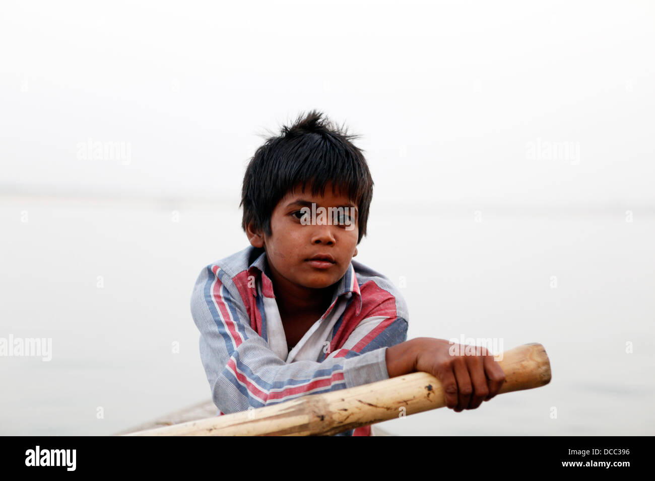 Ein kleiner Junge Zeilen ein Boot voller Touristen auf einer Tour entlang des Flusses Ganges, Varanasi, Indien Stockfoto