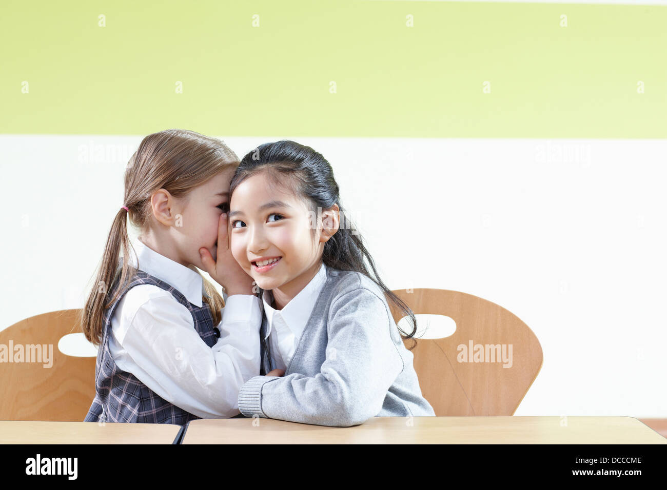 ein Mädchen flüsterte ihrer Freundin in einem Klassenzimmer Stockfoto