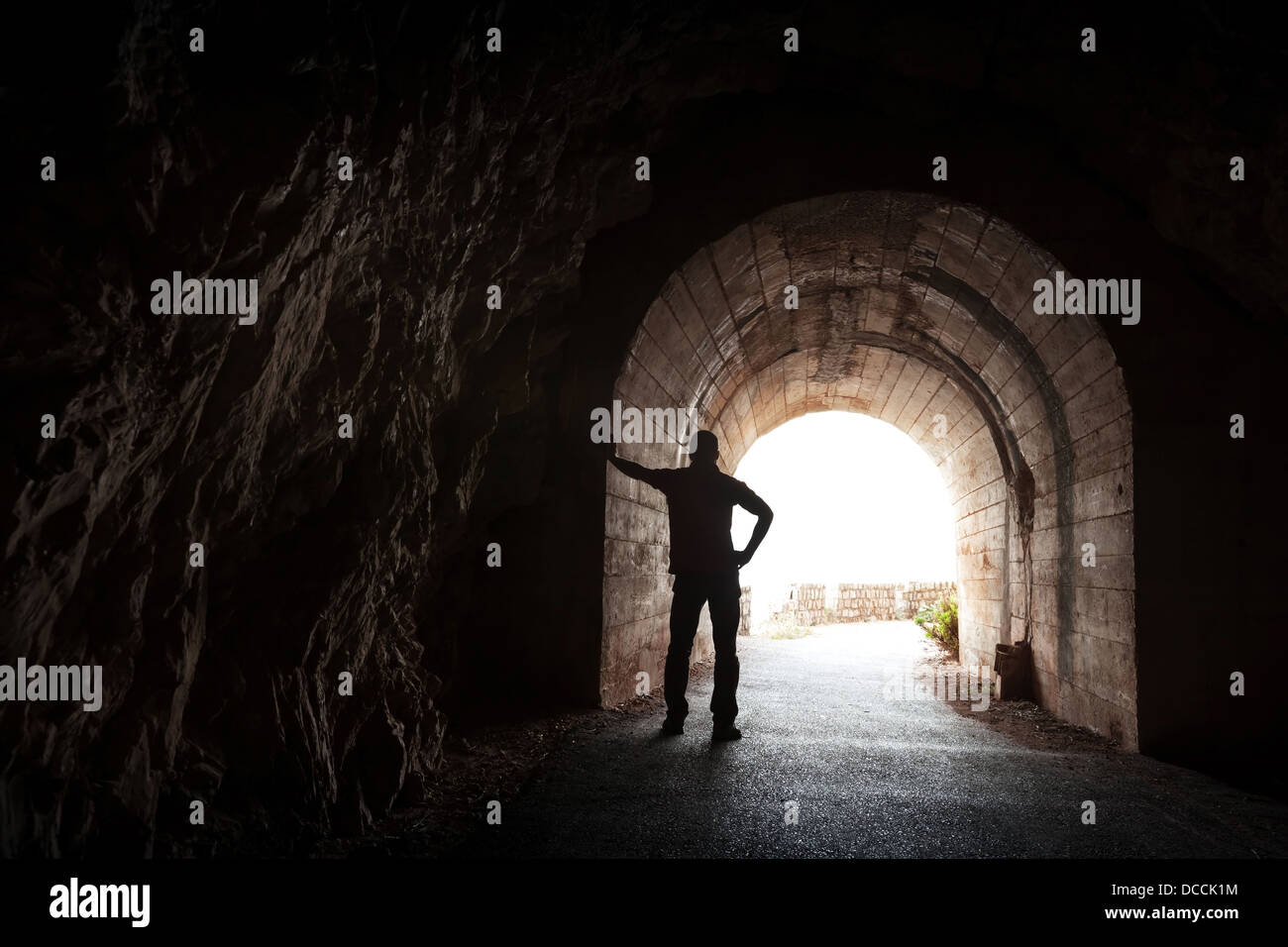 Junger Mann steht im dunklen Tunnel entspannt und sieht im Licht Stockfoto