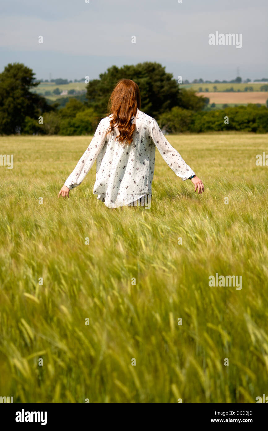Ein vertikales Bild einer jungen Frau mit langen roten Haaren, mit dem Rücken zur Kamera, in einem Feld von Weizen Stockfoto