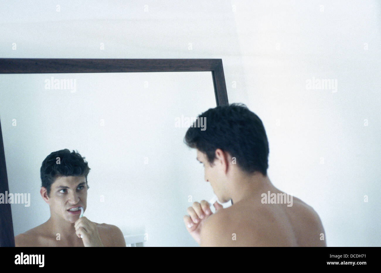 Junger Mann, seine Zähne putzen & suchen im Badezimmerspiegel