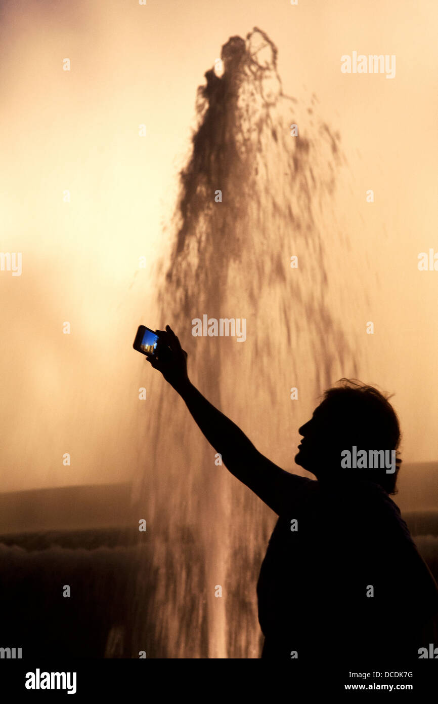 Frau, die ein Foto von den magischen Springbrunnen auf ihrem Kameratelefon macht. Stockfoto