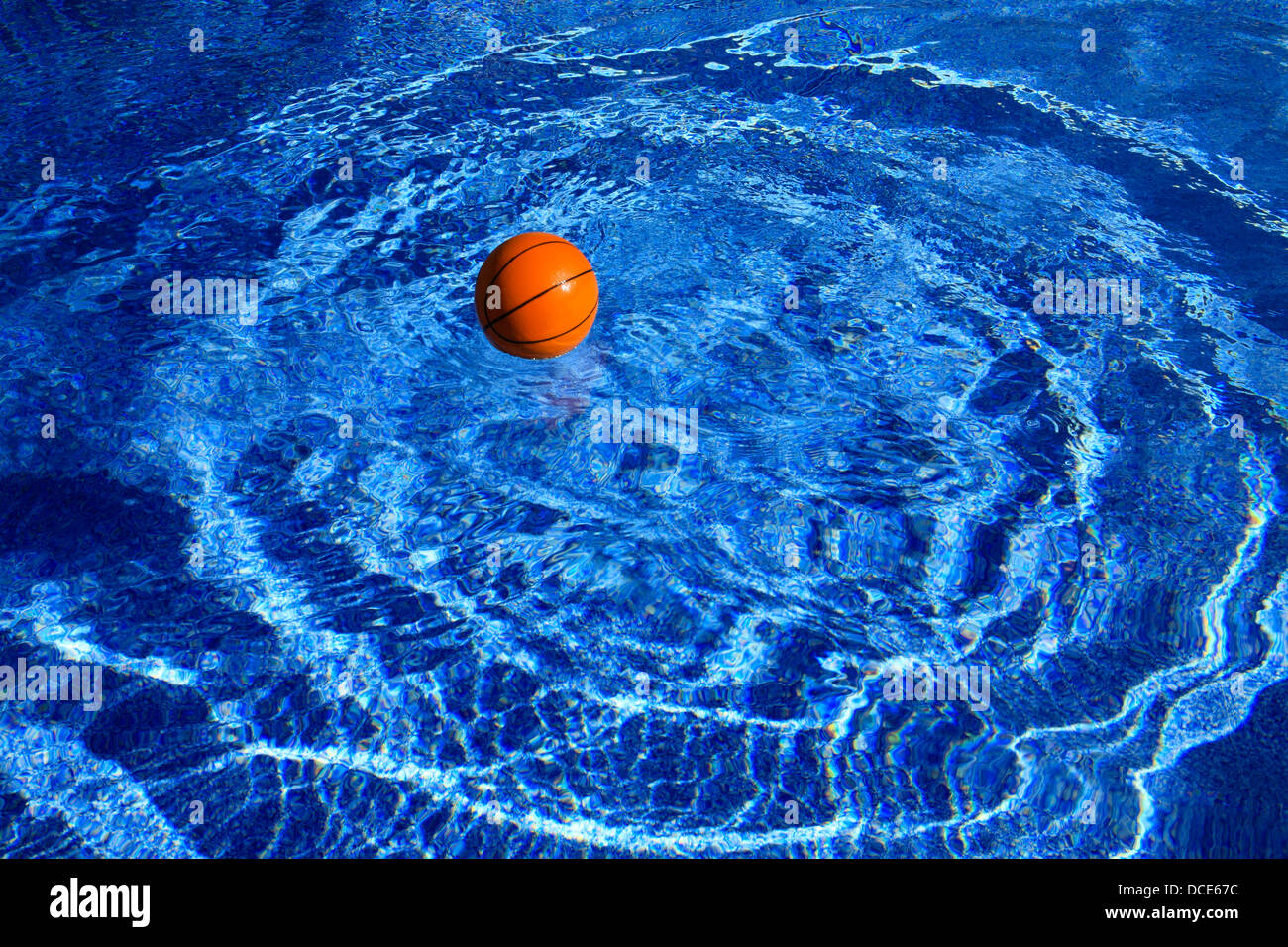 Ein Basketball schafft konzentrische Wellen im tiefblauen Schwimmbadwasser Stockfoto