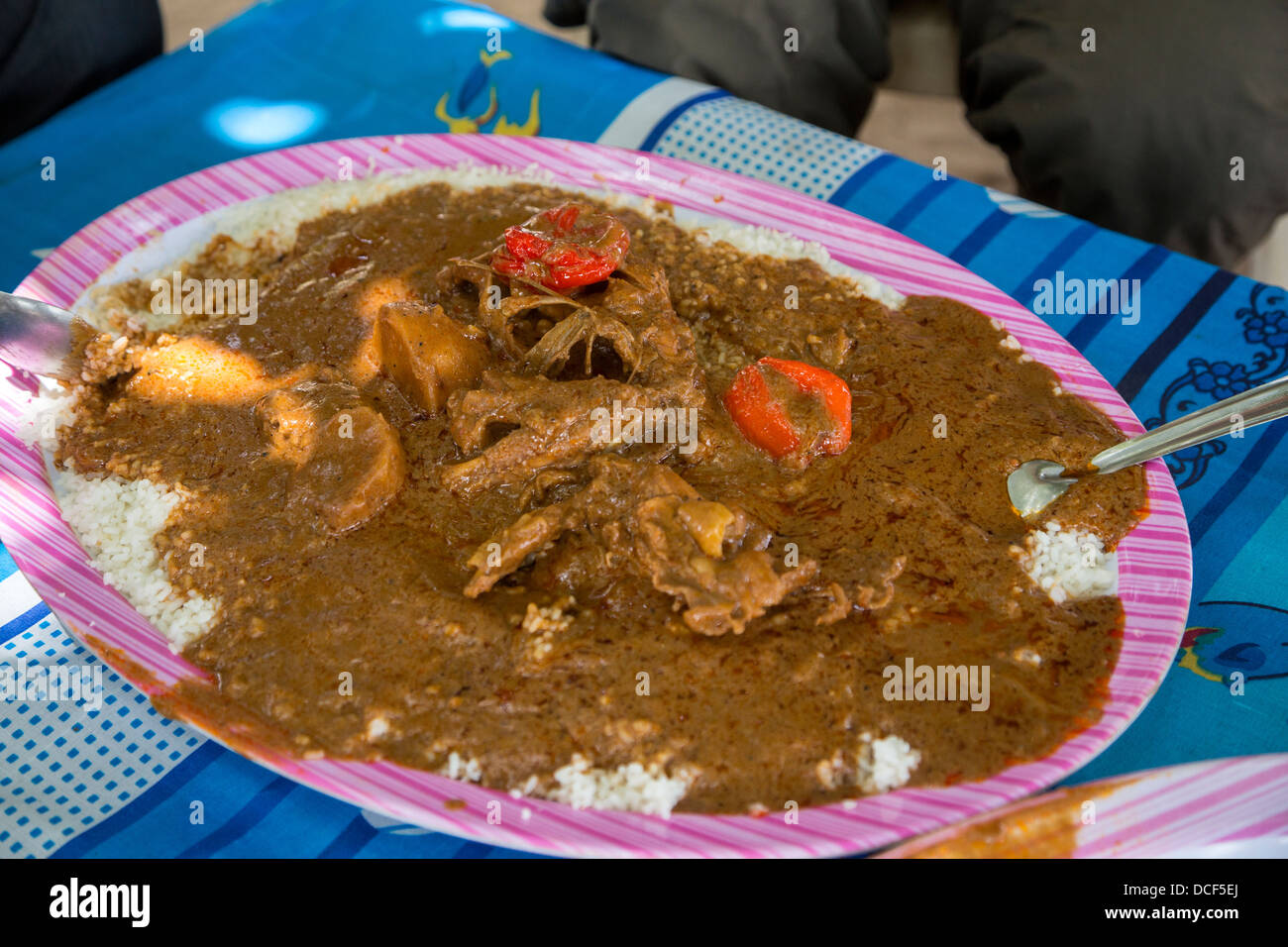 Cashew-Nuss-Eintopf mit Huhn, Paprika und Reis. Menschen rund um den Tisch essen aus einer gemeinsamen Schüssel.  Gambia. Stockfoto