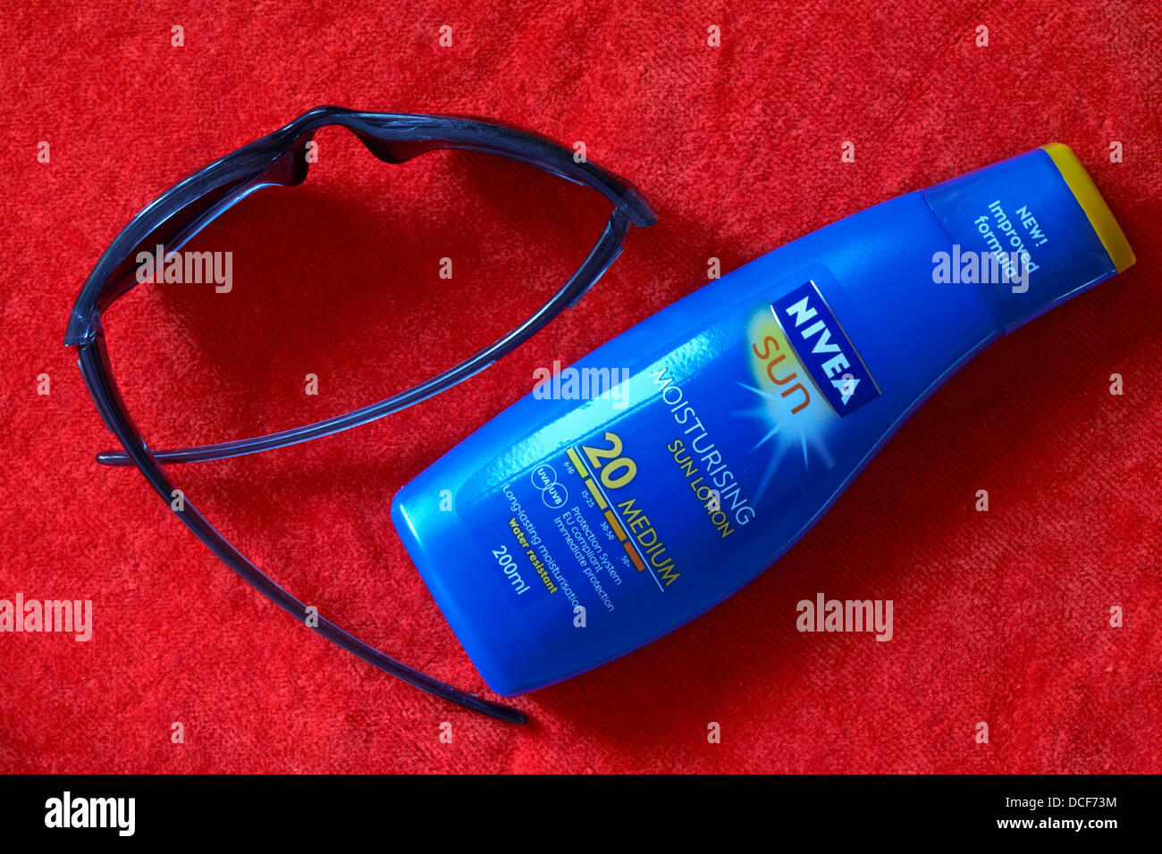 sonnenbrille und Flasche Nivea Sun feuchtigkeitsspendende Sonnenlotion Sonnencreme auf orangefarbenem Handtuch Nivea LSF 20 Stockfoto