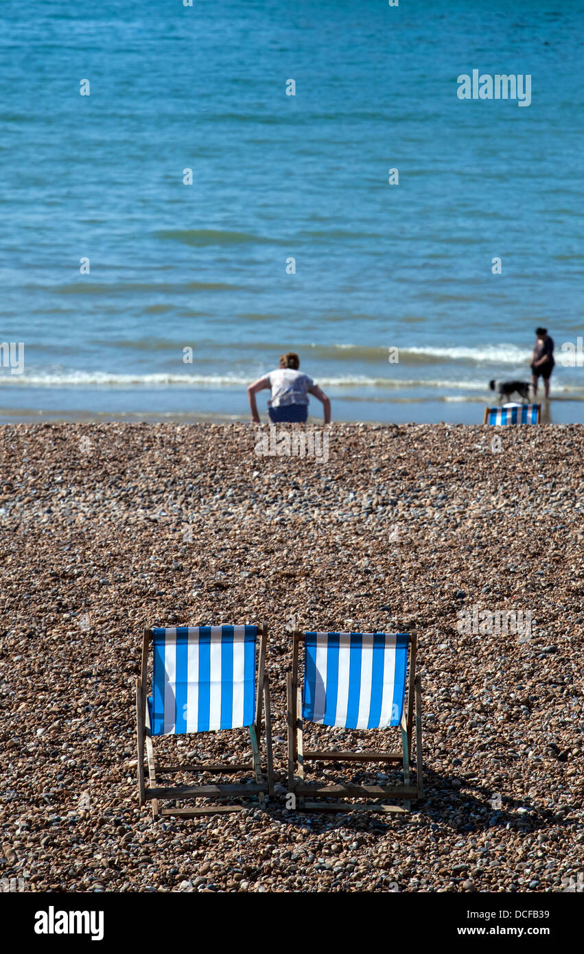 Leere Liegestühle mit Menschen Paddeln im Meer Stockfoto