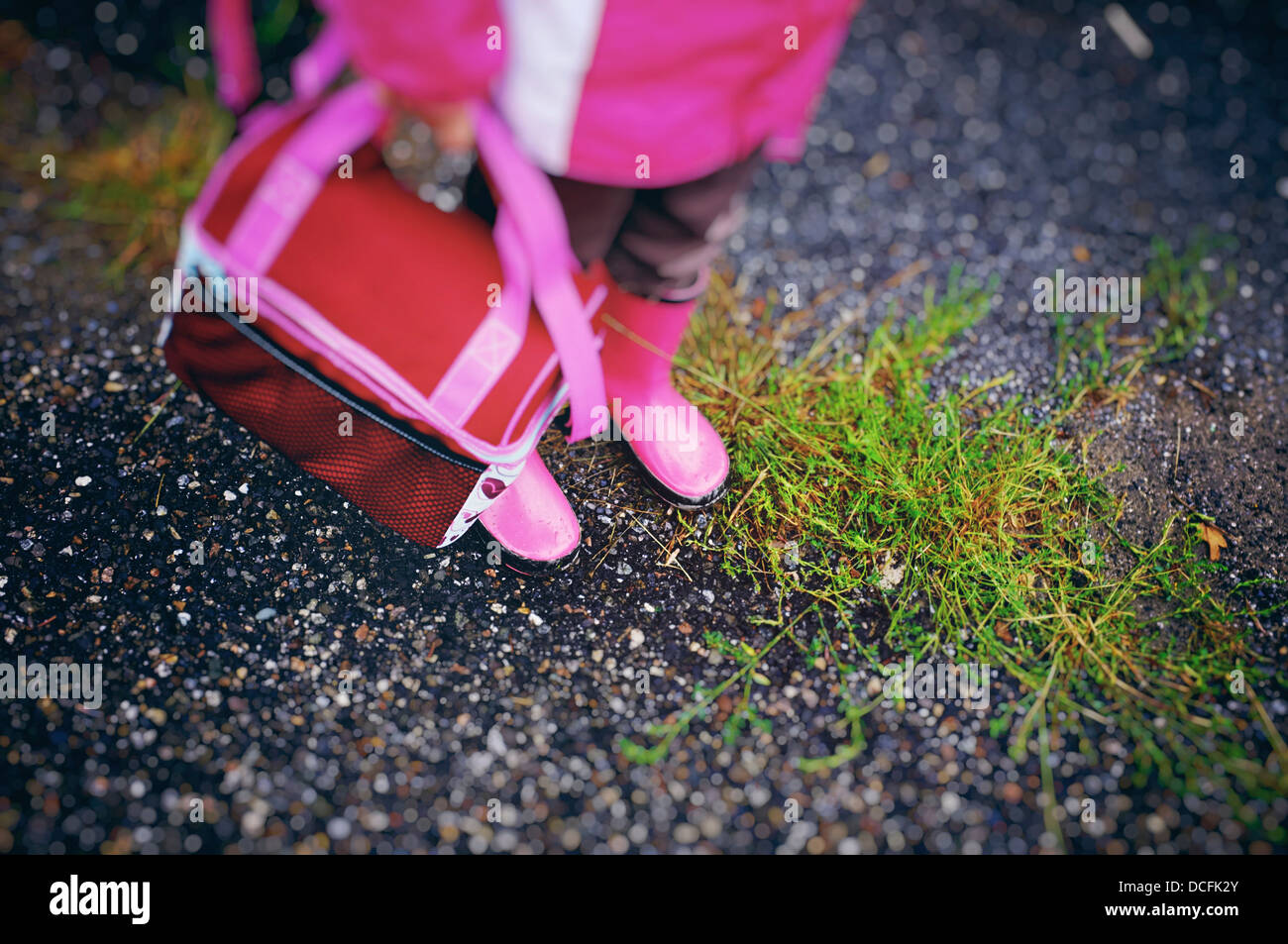 Mädchen die passenden rosa Stiefel, Mantel und Lunchpaket auf einer grasbewachsenen Straße Stockfoto