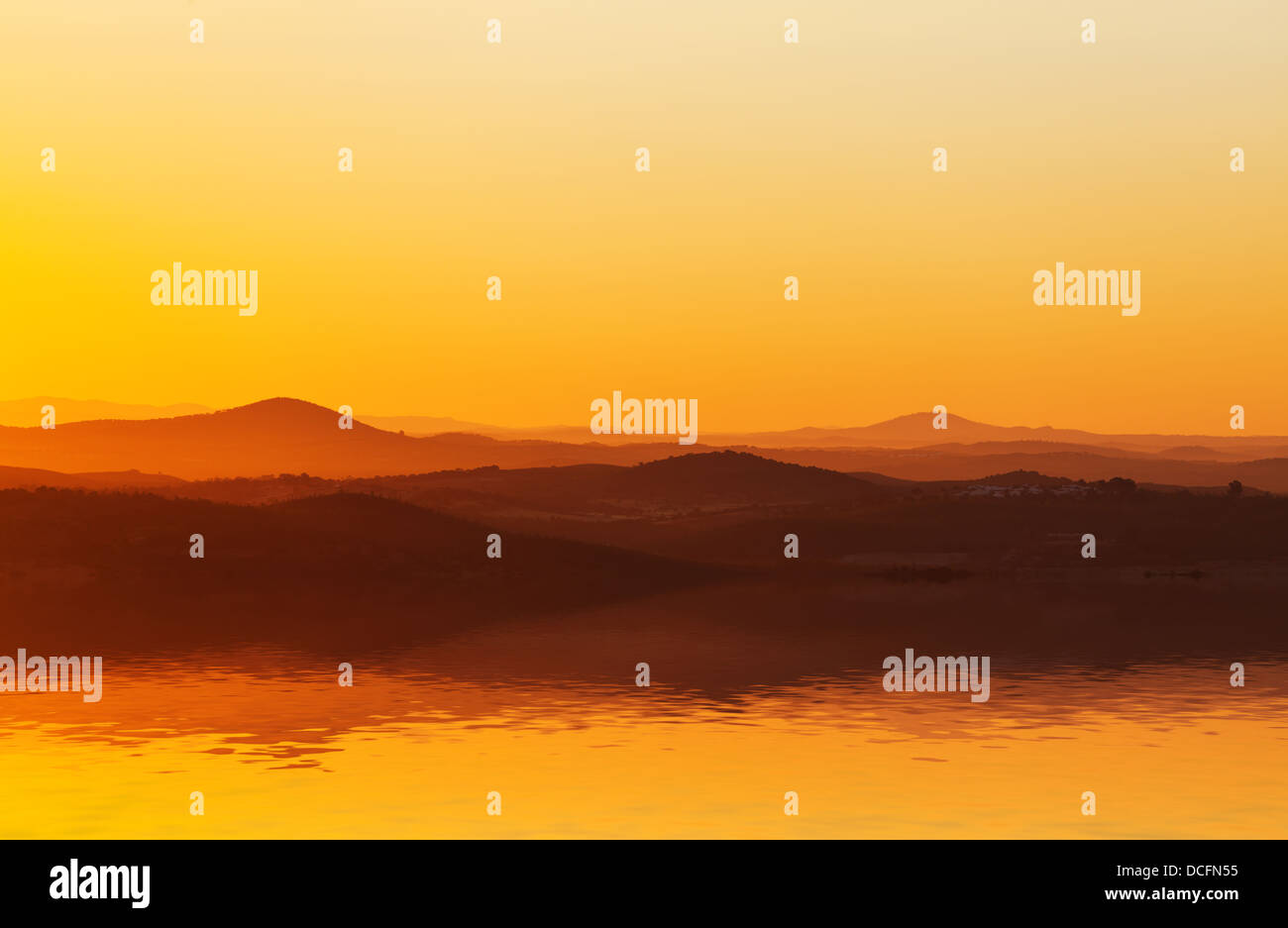 Spektakuläre orange sunset Einstellung hinter ein Mittelgebirge spiegelt sich in der Oberfläche des Wassers immer noch im Vordergrund Stockfoto