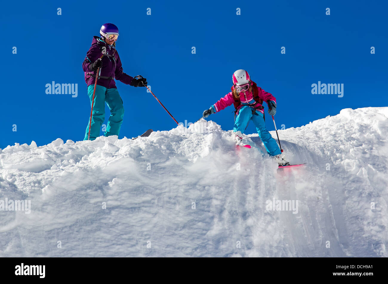 Kleine Mädchen und eine erwachsene Frau, Skifahren in den Bergen gegen den blauen Himmel. Bei sonnigem Wetter Stockfoto