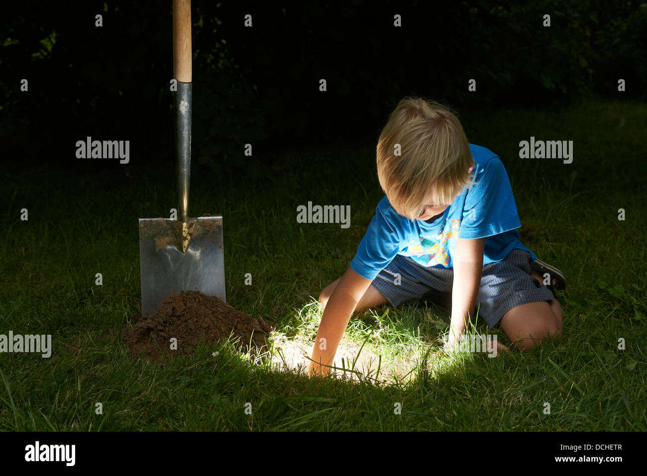Kind junge einen Schatz in magische Loch im Boden zu graben, in der Dämmerung Stockfoto