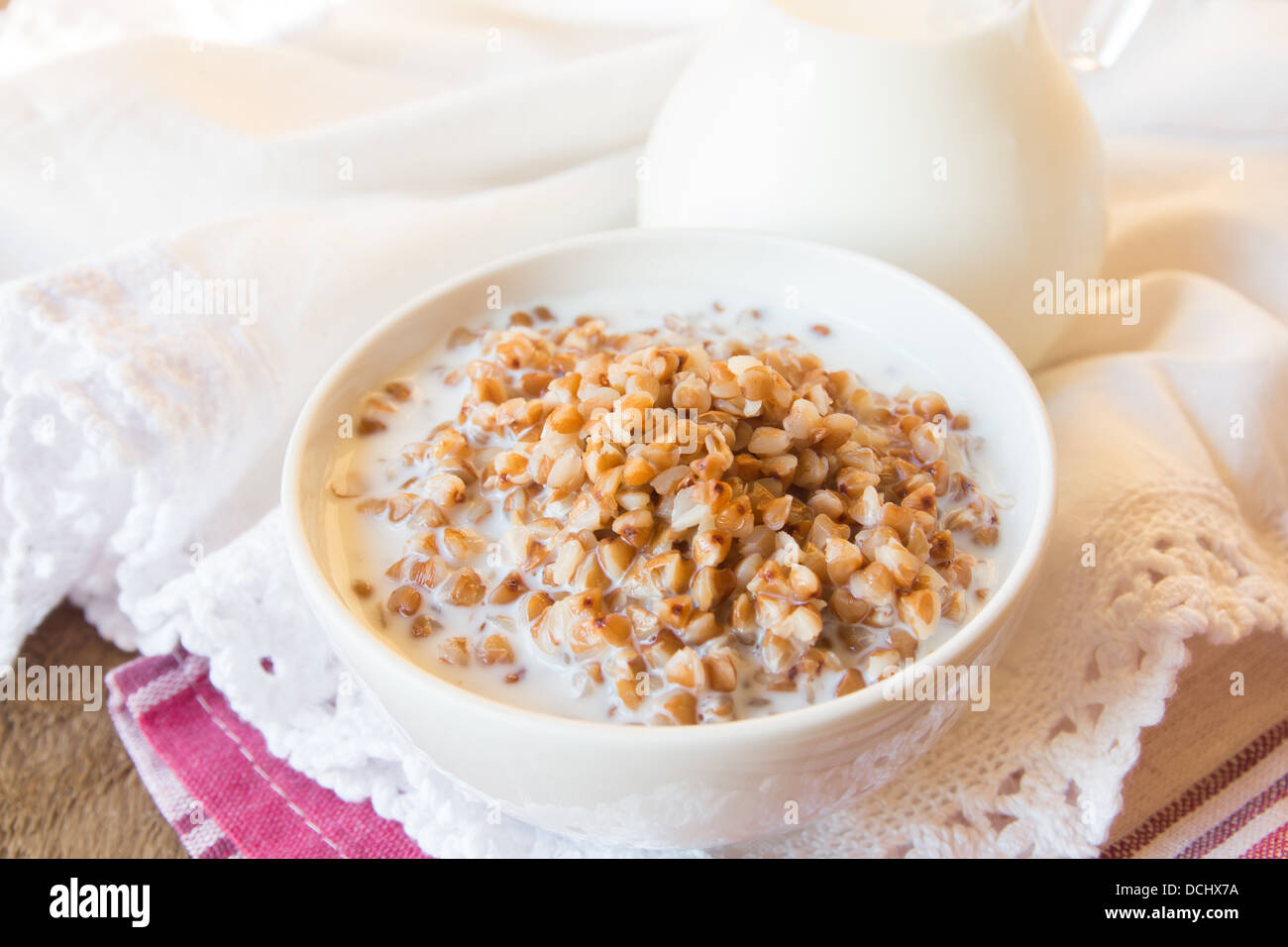 Buchweizengrütze mit Milch auf weiße Serviette und Holztisch, Nahaufnahme, horizontale. Natürliche Bio vegetarisches Essen (Frühstück) Stockfoto