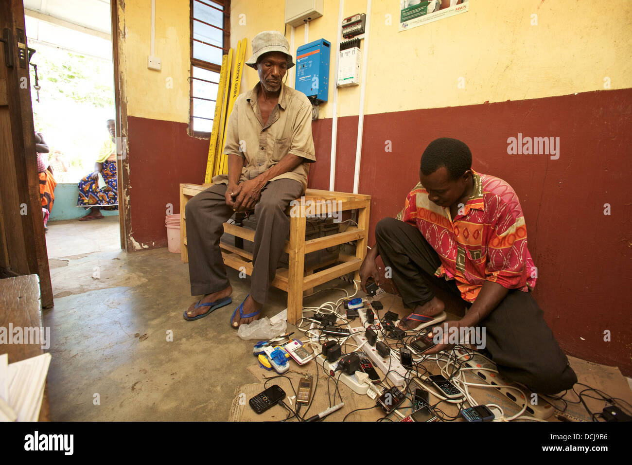 Tansanischen Mann wartet auf die Rückkehr von seinem Handy in einem solarbetriebenen Handy aufladen stand, Miono Region, Tansania. Stockfoto