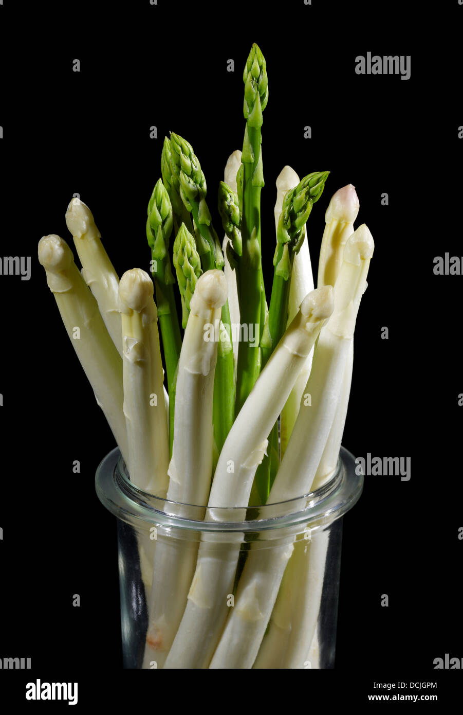 Glas gefüllt mit einem Bündel von weißem und grünem Spargel Gemüse in Schwarz zurück Stockfoto