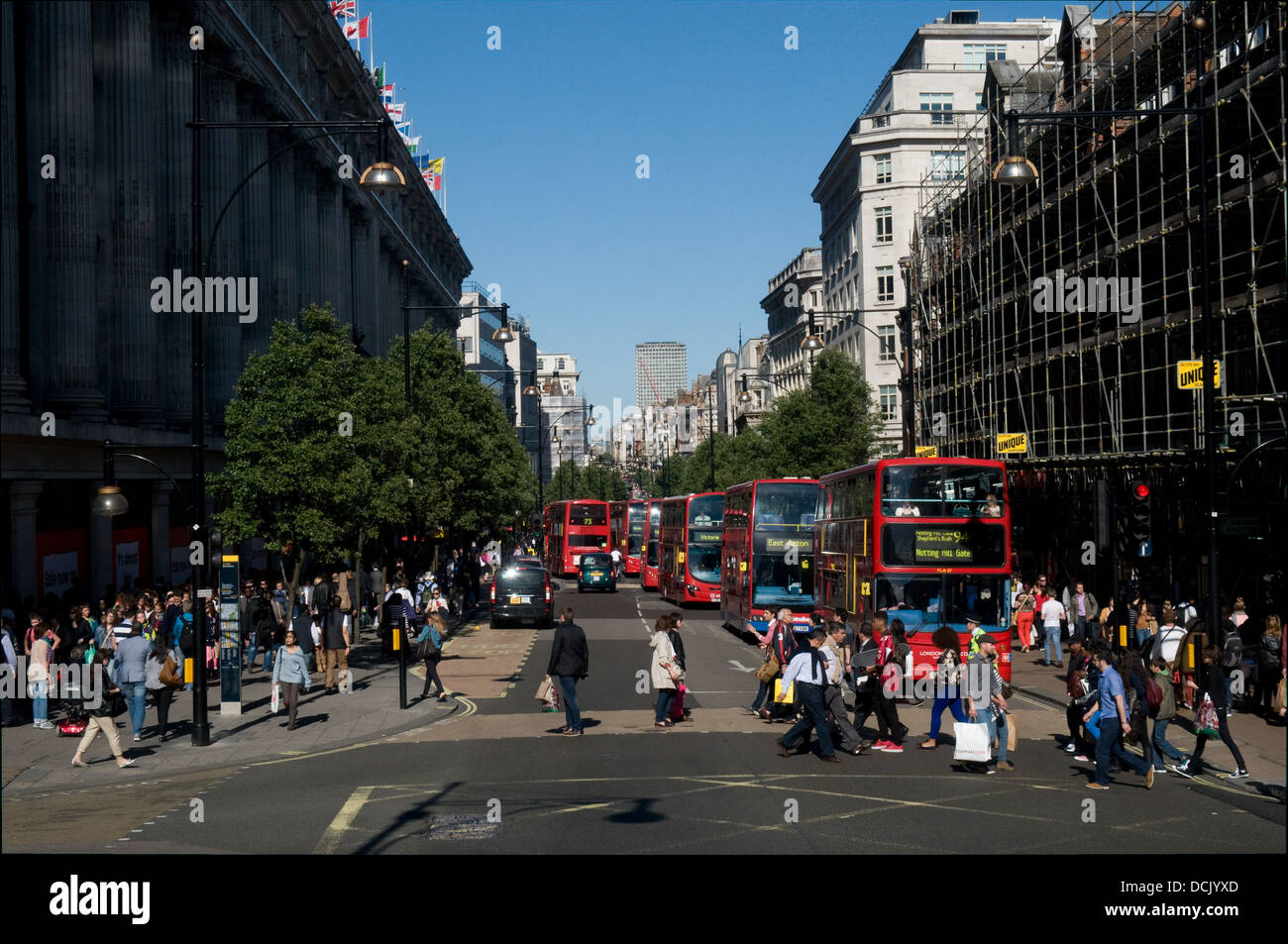 Tourist, Einkäufer und Arbeitnehmer überqueren Oxford Street in London an einem sonnigen Tag. Eine Reihe von Busse fahren auf der Straße. Stockfoto
