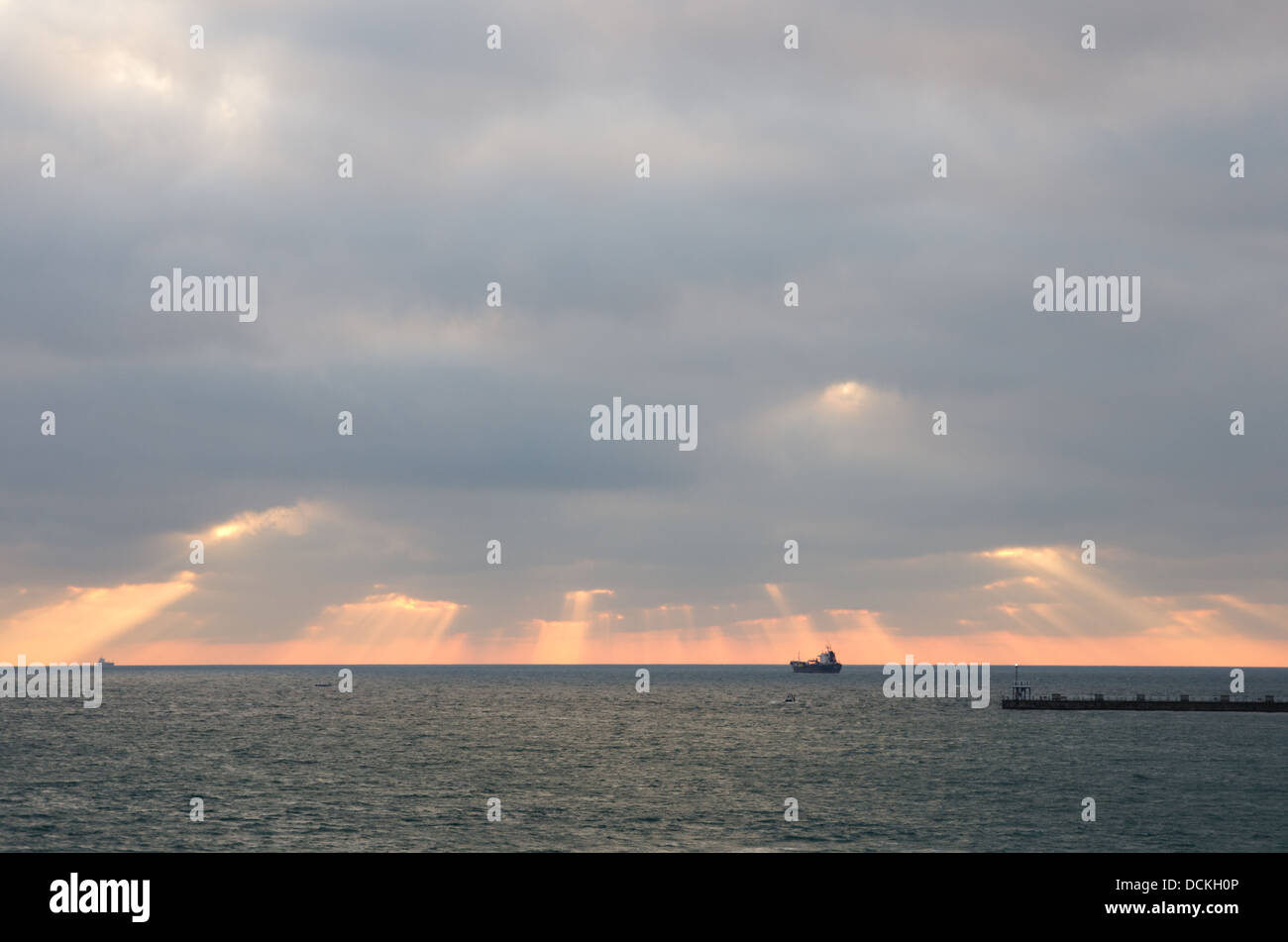 Ein Blick auf Ferne Schiffe unter grauen Wolken mit rosa morgendlichen Sonnenstrahlen versuchen zu durchbrechen. Stockfoto