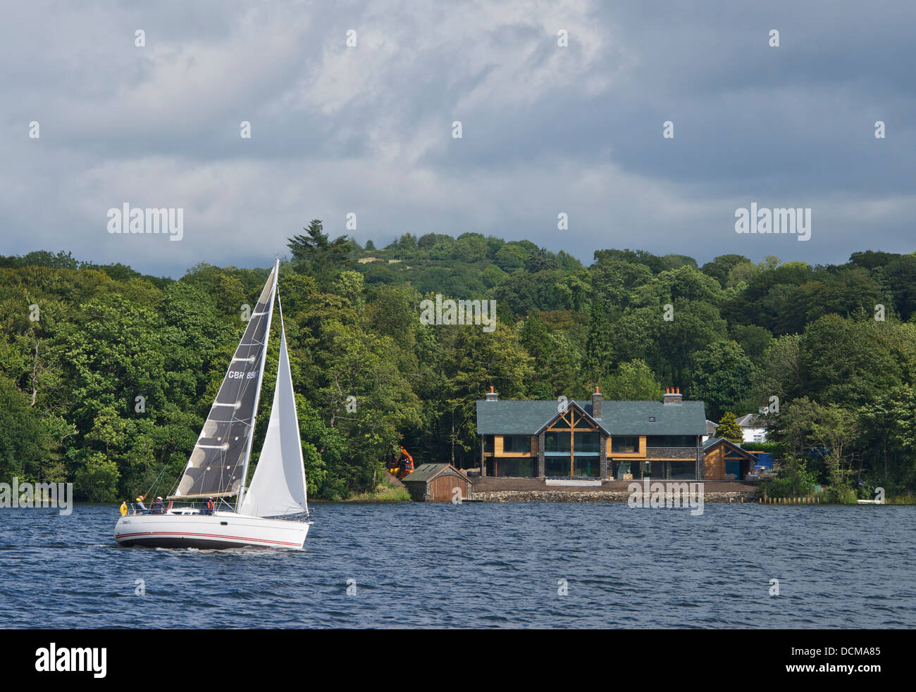 Segelboot vorbei Haus gebaut auf die Ufer des Lake Windermere, Lake District National Park, Cumbria, England UK Stockfoto