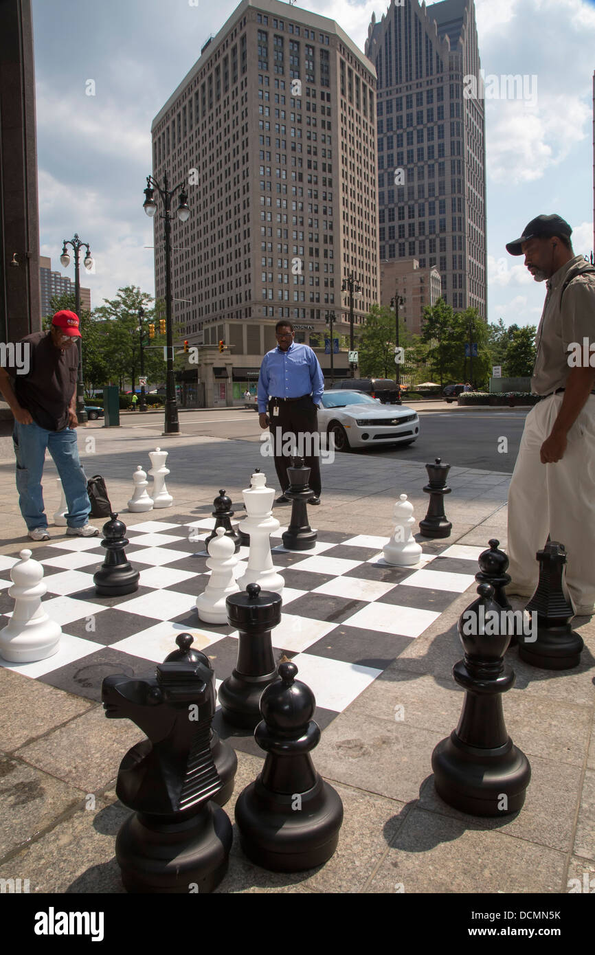 Detroit, Michigan - zwei Männer spielen Schach auf einem Bürgersteig Schachbrett in der Innenstadt von Detroit als Dritter Mann Uhren. Stockfoto