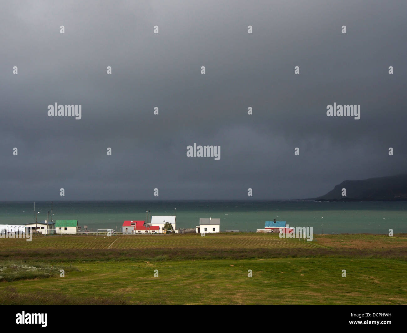 Dunkle Regenwolken über Häuser, Bakkagerði, Berggipfeln Eystri, Island Stockfoto