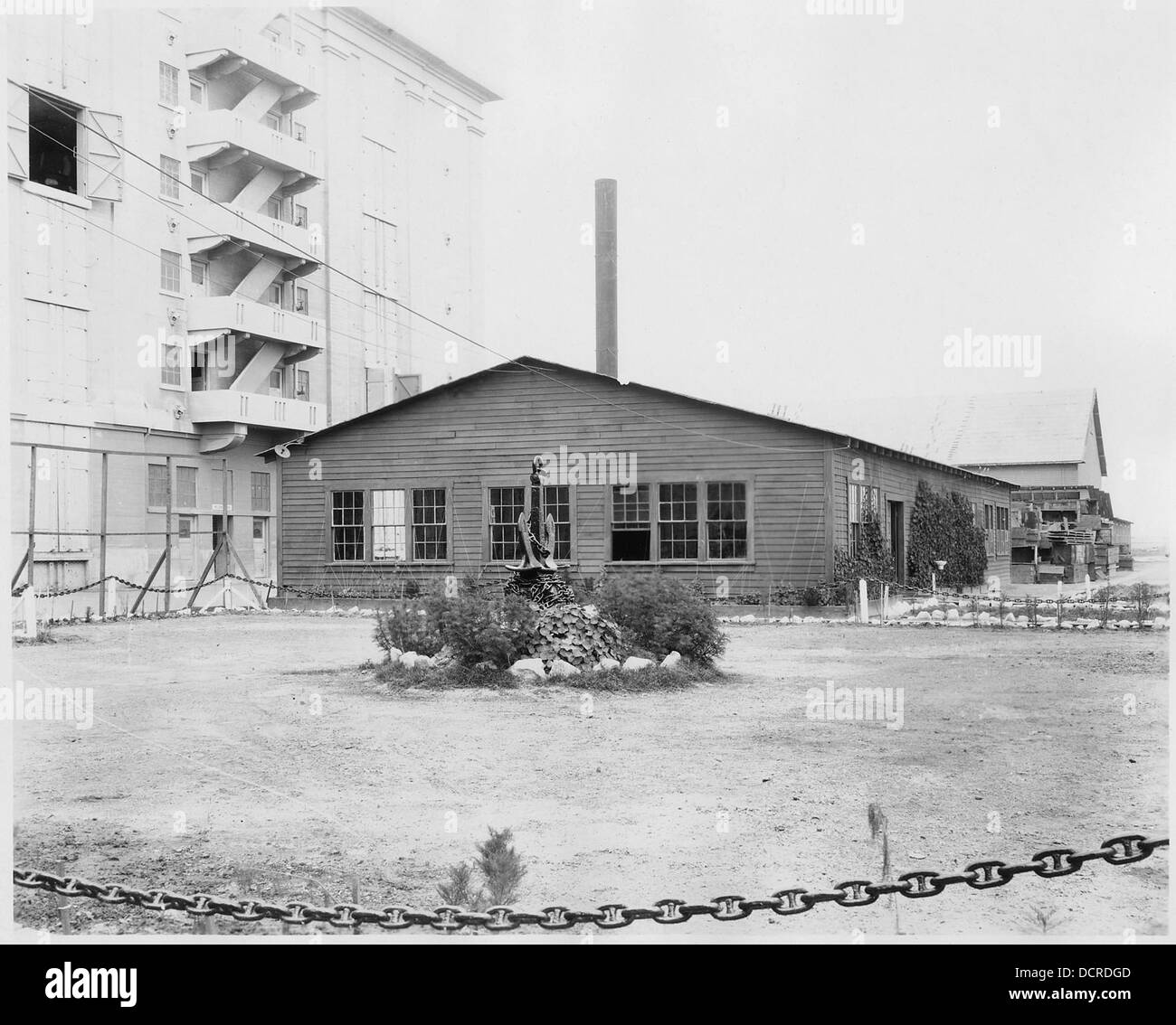 (Einstöckiges Holzgebäude neben einer neueren Kaserne. Im Vordergrund ist ein montierter Anker, der von Anker umgeben ist... - 295468 Stockfoto